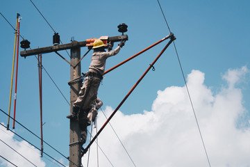 Two linemans use devices that are insulated for maintenance high voltage distribution system. To prevent power outages. The background is the sky.