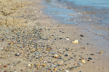 Fototapeta na wymiar Sandy beach with pebble and coming waves at the sea, close-up