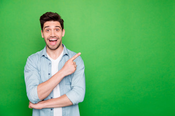 Photo of cheerful positive brown haired cute man pointing at empty space expressing shocked emotions excited ecstatic isolated over green vivid color background - obrazy, fototapety, plakaty