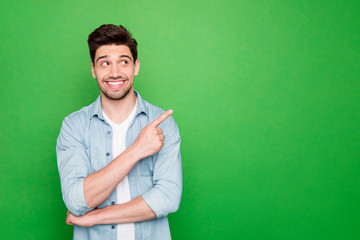 Photo of amazing salesman guy in excited mood indicating finger to empty space advising cool shopping prices wear casual denim shirt isolated green color background - obrazy, fototapety, plakaty