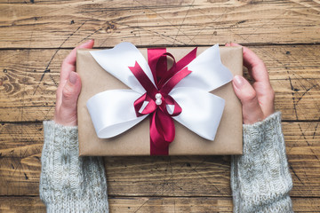 Gift or present box with a big bow in the hands of a woman in a sweater. Flatlay composition for Christmas birthday, mother day or wedding.