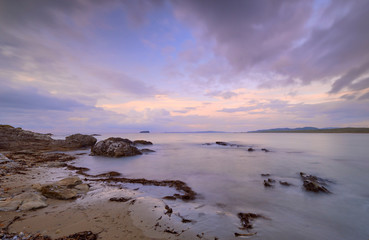 Mauve Sunset with wispy clouds on Pollan Beach, Inishowen, Ireland.  Featuring rocks algues and sand with viiew of Malin Peninsula on horizon