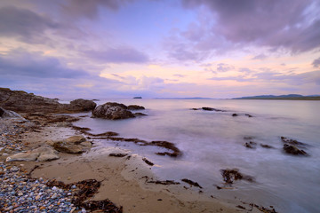 Mauve Sunset with wispy clouds on Pollan Beach, Inishowen, Ireland.  Featuring rocks algues and sand with viiew of Malin Peninsula on horizon