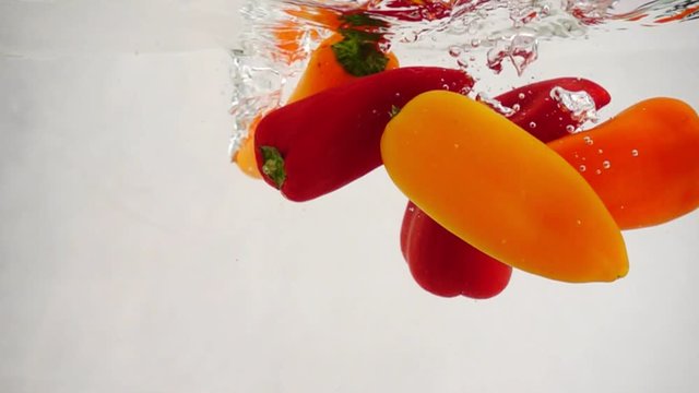 Lot fresh multicolored bell peppers falls into water with splashes and bubbles, slow motion close-up, on. Theme of vegetarianism and raw food as a lifestyle. Vegetable cocktail.