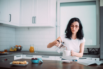 Beautiful young woman pouring coffee in the kitchen
