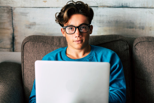 Portrait of handsome caucasian people teenager working with personal laptop computer at home sitting on the sofa - concept of student for high school or graduate or job search with modern technology