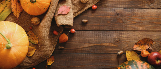 Autumn frame made of pumpkins, dried fall leaves, apples, red berries, walnuts, blanket on wooden table. Thanksgiving, Halloween, Autumn Harvest concept. Flat lay composition, top view, copy space
