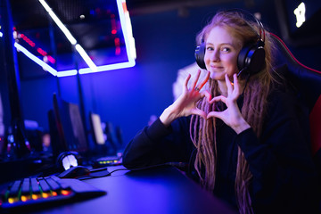 Streamer beautiful girl shows heart sign with hands professional gamer playing online games computer, neon color © Parilov