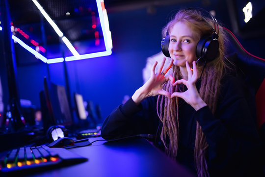 Streamer beautiful girl shows heart sign with hands professional gamer playing online games computer, neon color