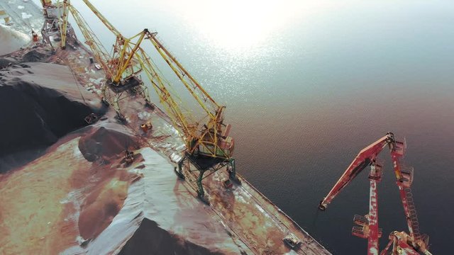 port cranes on the river bank produce sand. Port cranes with a bucket on the river bank. Extraction of river sand. Port cargo cranes extracts river sand, production. Sunset. Barge.