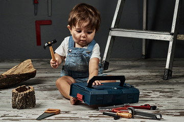 A baby playing with work tools and wood in a workshop