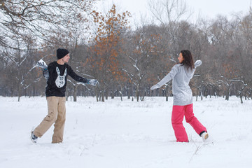 Fototapeta na wymiar Loving couple having fun, laughing, playing and throwing snowballs in a winter park. A boyfriend and a girl friend spend winter time together.