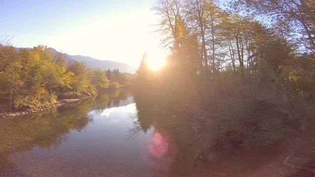 4K AERIAL Setting sun peeking through the lush greenery along the banks of the mountain river