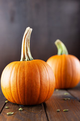 Ripe orange pumpkins and seeds on a dark wooden background.