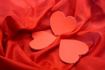 Three red hearts on red silk background with ripples.