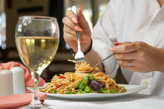 Young woman having spaghetti and a glass of white wine in the restaurant