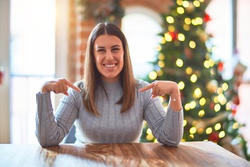 Young beautiful woman sitting at the table at home around christmas tree and decoration looking...