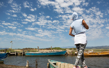 Chica con capucha de espaldas en un lado mirando el cielo y las barcas abandonadas 