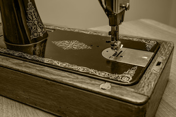 A vintage hand sewing machine in sepia tone