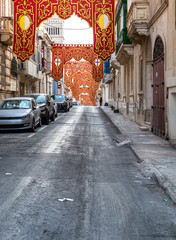 Street in Sliema, Malta, decorated with red religious ornate banners for village feast (festa) of St Gregory the Great.