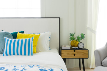 Bright bedroom interior with striped pillow on bed and bedside table lamp with picture frame on it. 