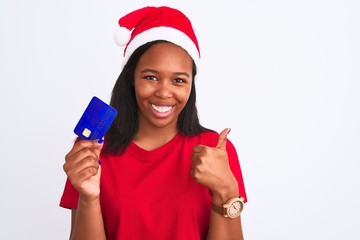 Young african american woman wearing christmas hat and holding credit card happy with big smile doing ok sign, thumb up with fingers, excellent sign