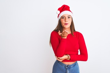 Young beautiful girl wearing Christmas Santa hat standing over isolated white background looking at the camera blowing a kiss with hand on air being lovely and sexy. Love expression.
