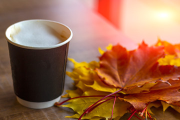 A cup of coffee and autumnal bouquet of yellow and orange maple leaves on wooden table in cafe close up. Going to cafe to warm up and have a snack on a cold autumn day.