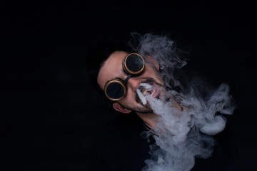 chico de lado echando humo por la nariz con gafas de steampunk puestas sobre un fondo negro