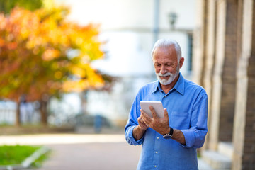 Portrait of a senior businessman using tablet. Senior man websurfing on tablet outdoors. Old man...