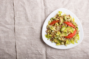 Vegetarian salad of celery, germinated rye, tomatoes and avocado on linen tablecloth, top view.