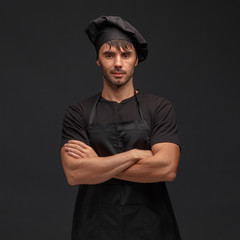 Young male cook in a black apron and hat.