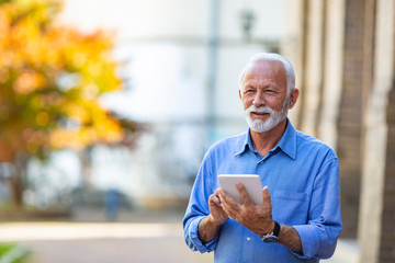 Senior man using a digital tablet outdoors. Business, technology and people concept - Senior businessman with tablet pc computer. Friendly handsome old man with tablet computer