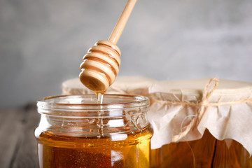 Pouring aromatic honey into jar, closeup. Honey in glass jars and honeycombs wax on wooden background. Wooden stick , instruments