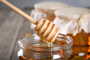 Pouring aromatic honey into jar, closeup. Honey in glass jars and honeycombs wax on wooden background. Wooden stick , instruments