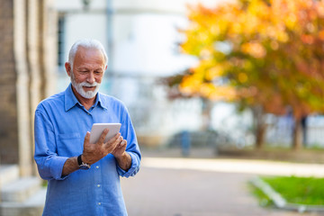 Senior man in town, working on tablet. Older man using tablet computer in park. Business, technology and people concept - Senior businessman with tablet pc computer