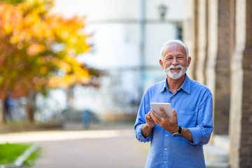 Senior man in town, working on tablet. Older man using tablet computer in park. Business, technology and people concept - Senior businessman with tablet pc computer