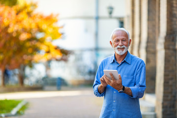 Senior man uses his digital tablet. Happy senior man holding digital tablet. Senior businessman using touchpad at outdoor. Senior businessman holding touchpad