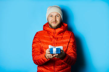 Man in a hat and a red jacket holds a gift on a blue background. Christmas present, holiday, winter holidays, winter