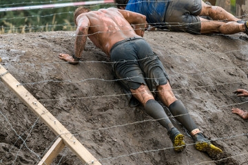 A man crawling under barbed wire at an obstacle course race