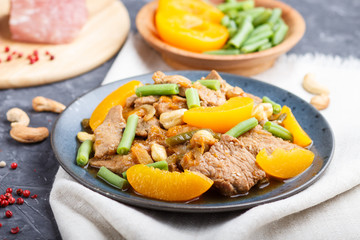 Fried pork with peaches, cashew and green beans on a black concrete background, close up, side view.