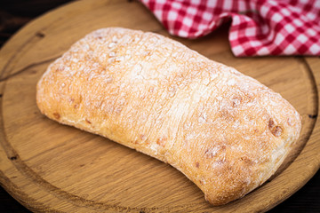 Loaf of ciabatta bread on a cutting board on the dark wooden table