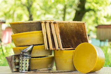 Large round pieces of natural beeswax on the background of beehives in the garden. Large round pieces of beeswax, bee smoker and beekeeper's tool on the background of beehives in the garden.