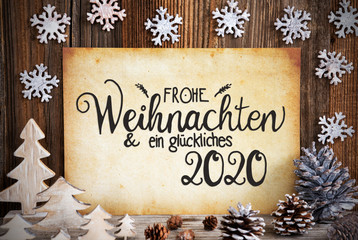 Fototapeta na wymiar Old Paper With German Text Frohe Weihnachten Und Ein Glueckliches 2020 Means Merry Christmas And Happy 2020. Christmas Decoration Like Tree, Fir Cone And Snowflakes. Brown Wooden Background