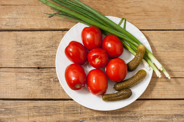 Fermented food on a white plate on an old wooden table. Pickled tomatoes and cucumbers. Salt for the winter. Traditional snack for alcohol.Top view