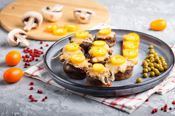 stuffed fried champignons with cheese, kumquats and green peas on a gray concrete background. side view, close up.