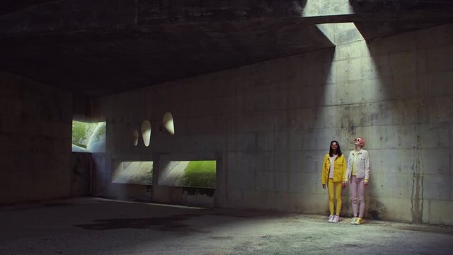 Two fashionable women standing inside of an abandoned building
