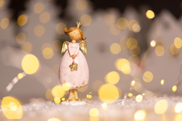 Decorative Christmas-themed figurines. Statuette of a Christmas angel. Christmas tree decoration. Festive decor, warm bokeh lights.