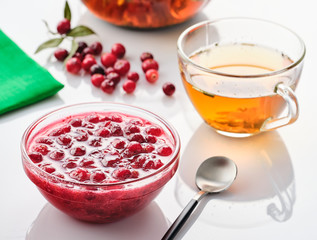 Cranberry jam in a glass bowl and teapot on a white background.