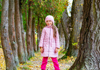 a little girl laughs and plays in the fall in nature with fallen leaves, walking in the fresh air in the Park with large trees